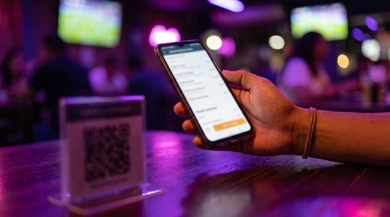 Una mano sostiene un celular con el menú digital sobre la mesa